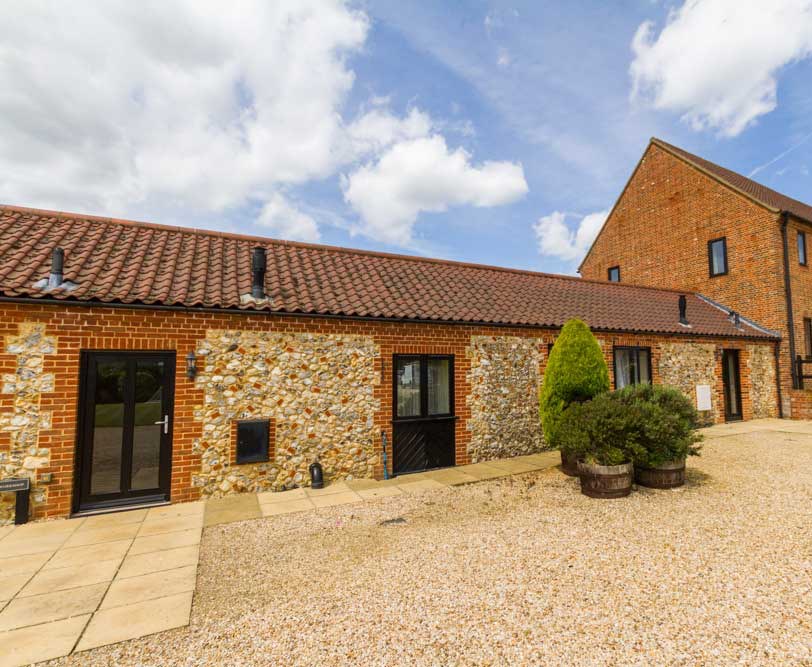 Enjoy the wonderful views across the fields towards Bircham Windmill from this spacious single storey cottage for 6.

It benefits from ample parking right outside the cottage and level access in and around the cottage to the paved garden area at the back and communal grassy area.

The sunny, light and spacious living area is designed for both the able and disabled user.

The open plan kitchen and dining space is fully equipped with everything you need including – oven, fridge/freezer, microwave, dishwasher, low level hob unit and some low level units integrated with normal height units.

Watch the sunset from the spacious sitting room complete with comfortable seating and TV/DVD player. Patio doors open out onto the garden seating area where you can soak up the view.

There are three bedrooms, one king size bed room and two twin bed rooms. The twin rooms share access to a large roll-in shower room with toilet and wash basin.

There is also a second roll-in shower room with toilet and wash basin.  It is fully centrally heated and has its own enclosed garden and patio area.